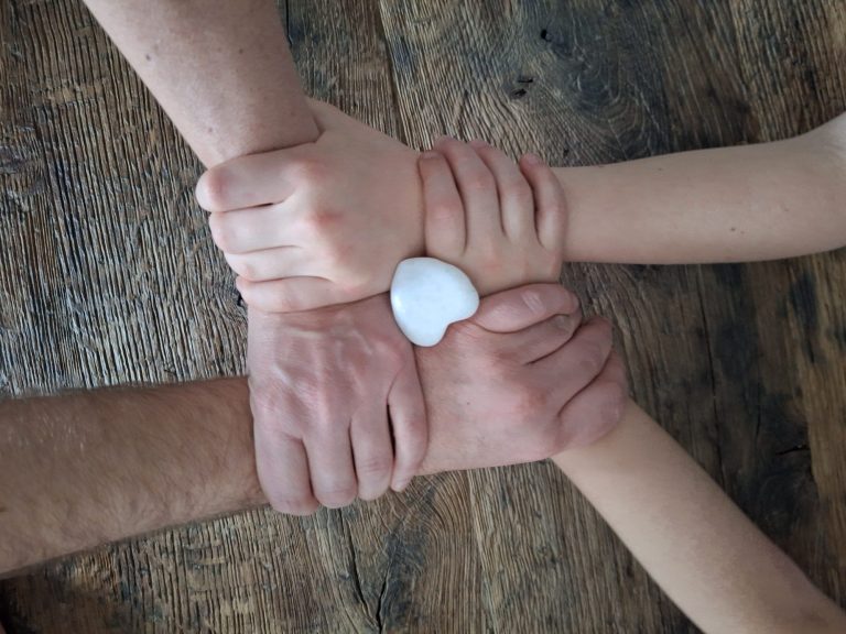 Samen sta je sterker; verbinding en liefde. Coach en therapeut. Verschillende handen die een hartvormige steen vasthouden op een houten oppervlak. Coach en therapeut.